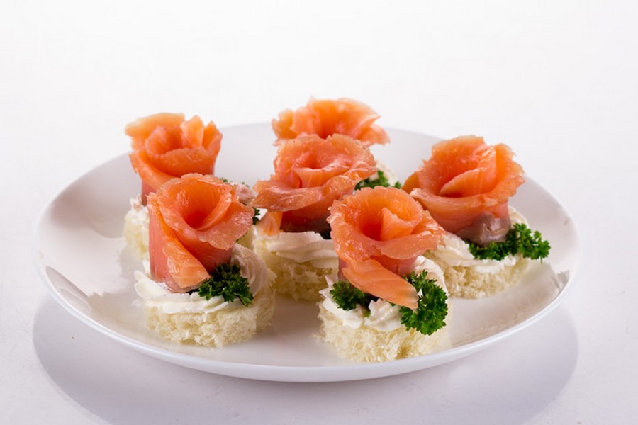 Троянди з червоної слабосоленої риби, вершкового сиру та зелені на шматочках білого хліба або багета.